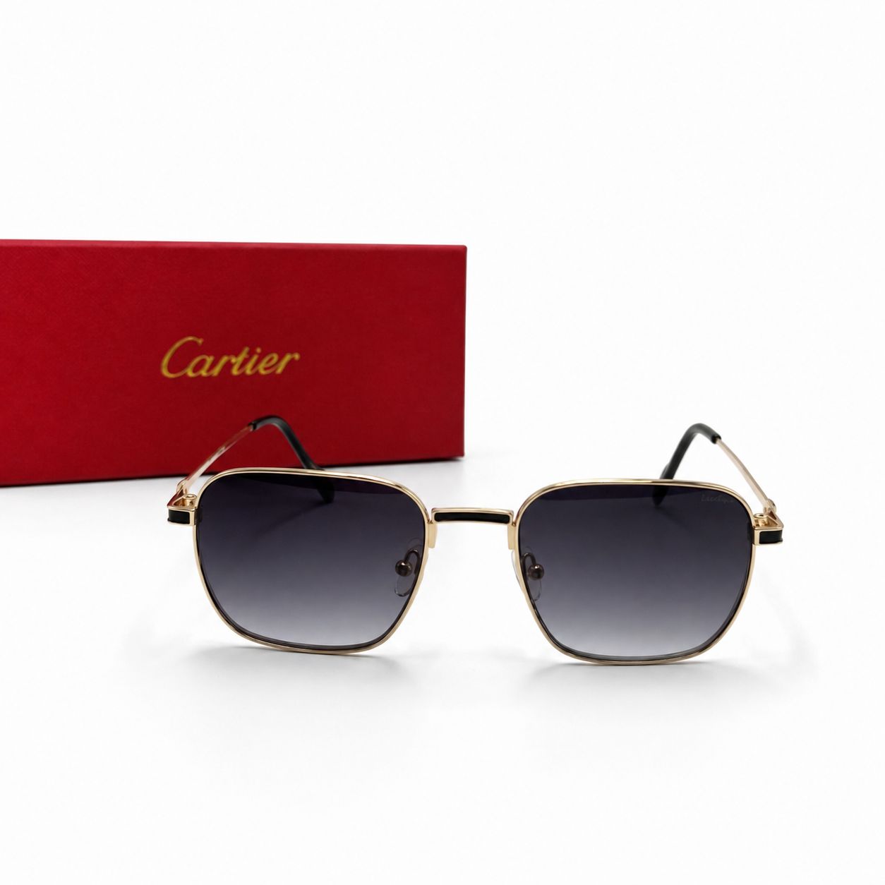 Lunettes de soleil de luxe Cartier avec monture en métal doré et liseré en laque noire, verres foncés et charnières dorées Signature C de Cartier, posées à côté de leur boîte rouge emblématique.