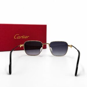 Lunettes de soleil de luxe Cartier avec monture en métal doré et liseré en laque noire, verres foncés et charnières dorées Signature C de Cartier, posées à côté de leur boîte rouge emblématique.